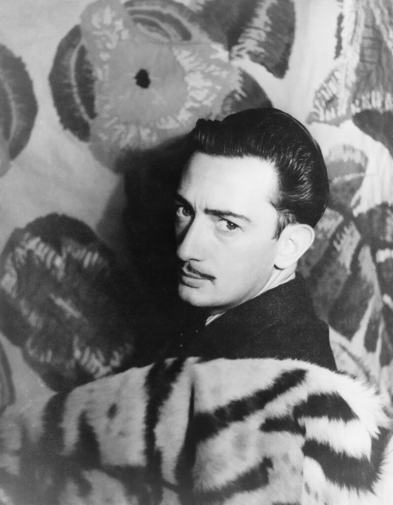 Black and white photograph of Salvador Dali with a discerning gaze, featuring his iconic slicked-back hair and mustache, set against a backdrop of his surrealist artwork.