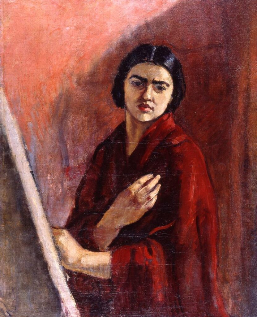 Amrita Sher-Gil self-portrait from 1930, showcasing the artist in a red robe with an intense gaze, against a rosy background, highlighting her bold style and the introspective nature of her work.