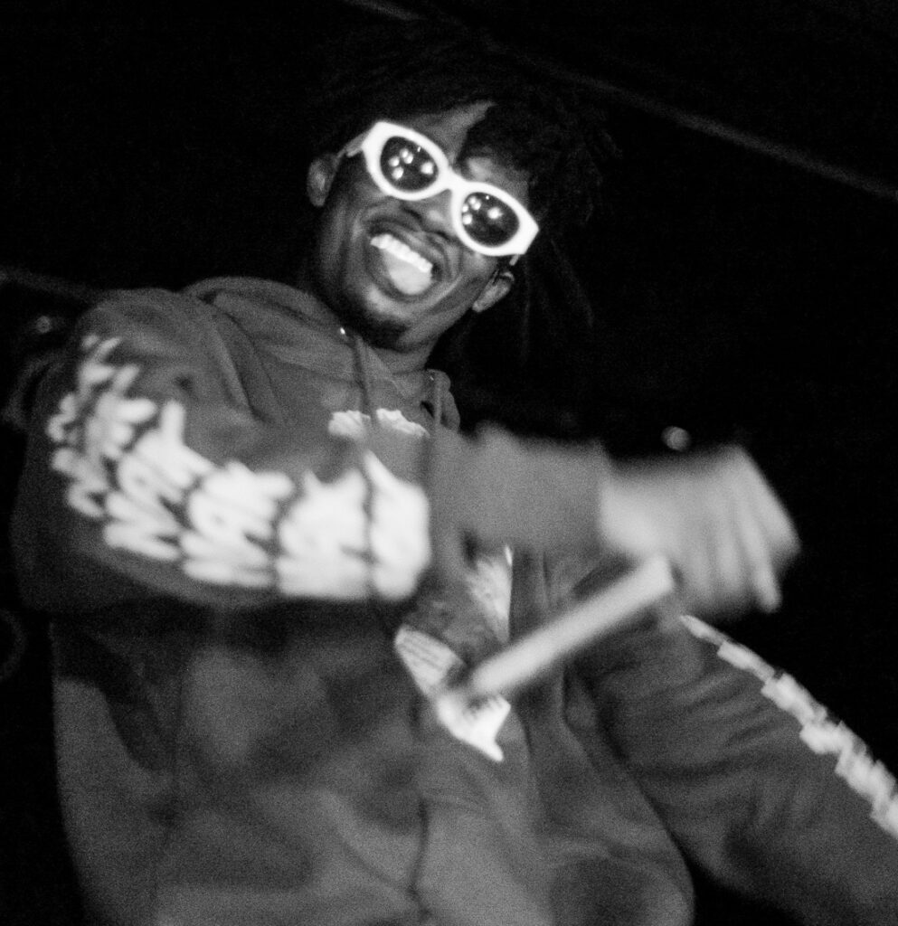 Playboi Carti performing live in 2016, wearing white sunglasses and a hoodie.