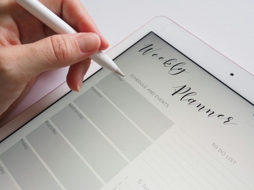 Close-up of a hand using a stylus on a digital tablet displaying a weekly planner page.