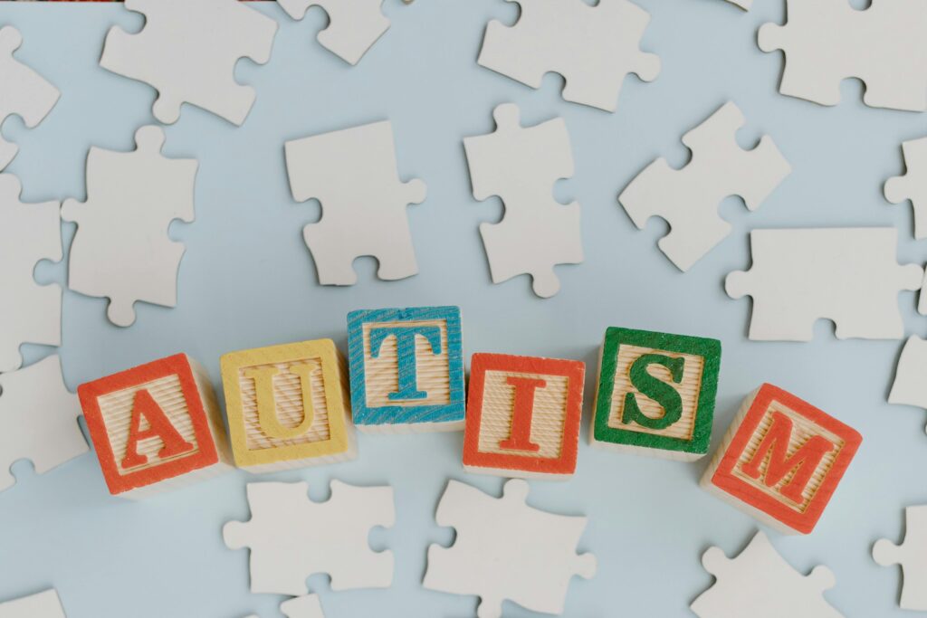 Colorful wooden blocks spelling 'autism' on a light blue background with scattered puzzle pieces.