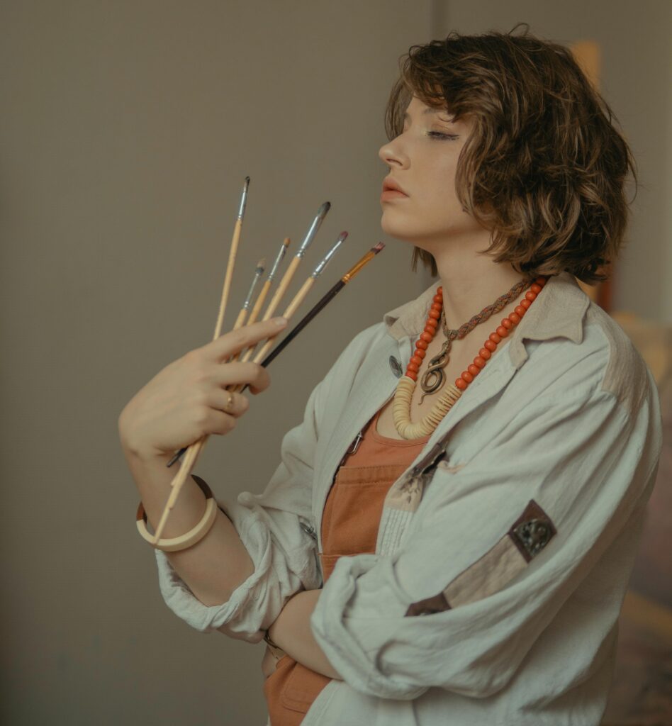 Artist experiencing art block, holding paintbrushes with a thoughtful expression.